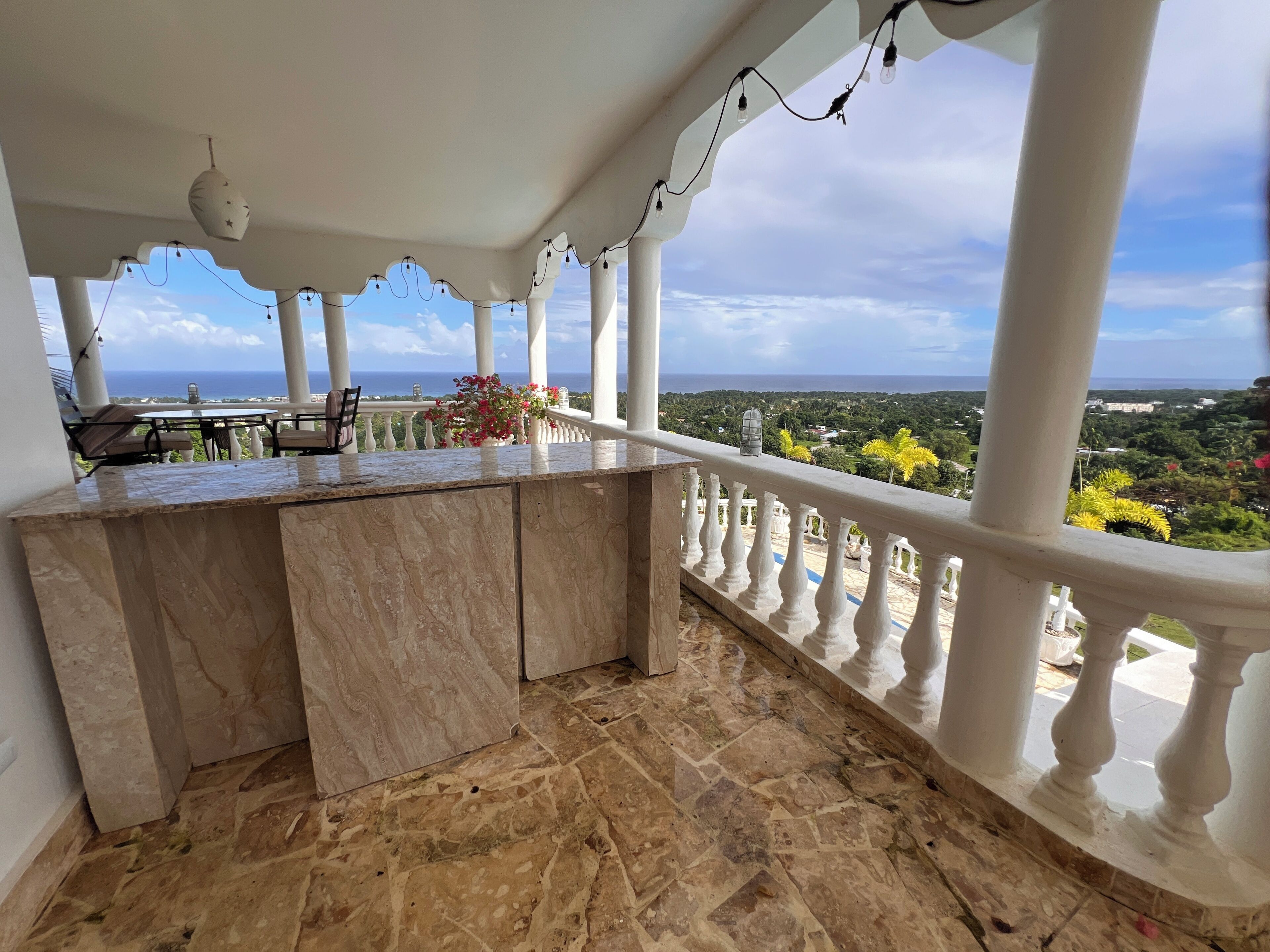 A balcony with a marble counter, white balustrades, and a view of the sea.