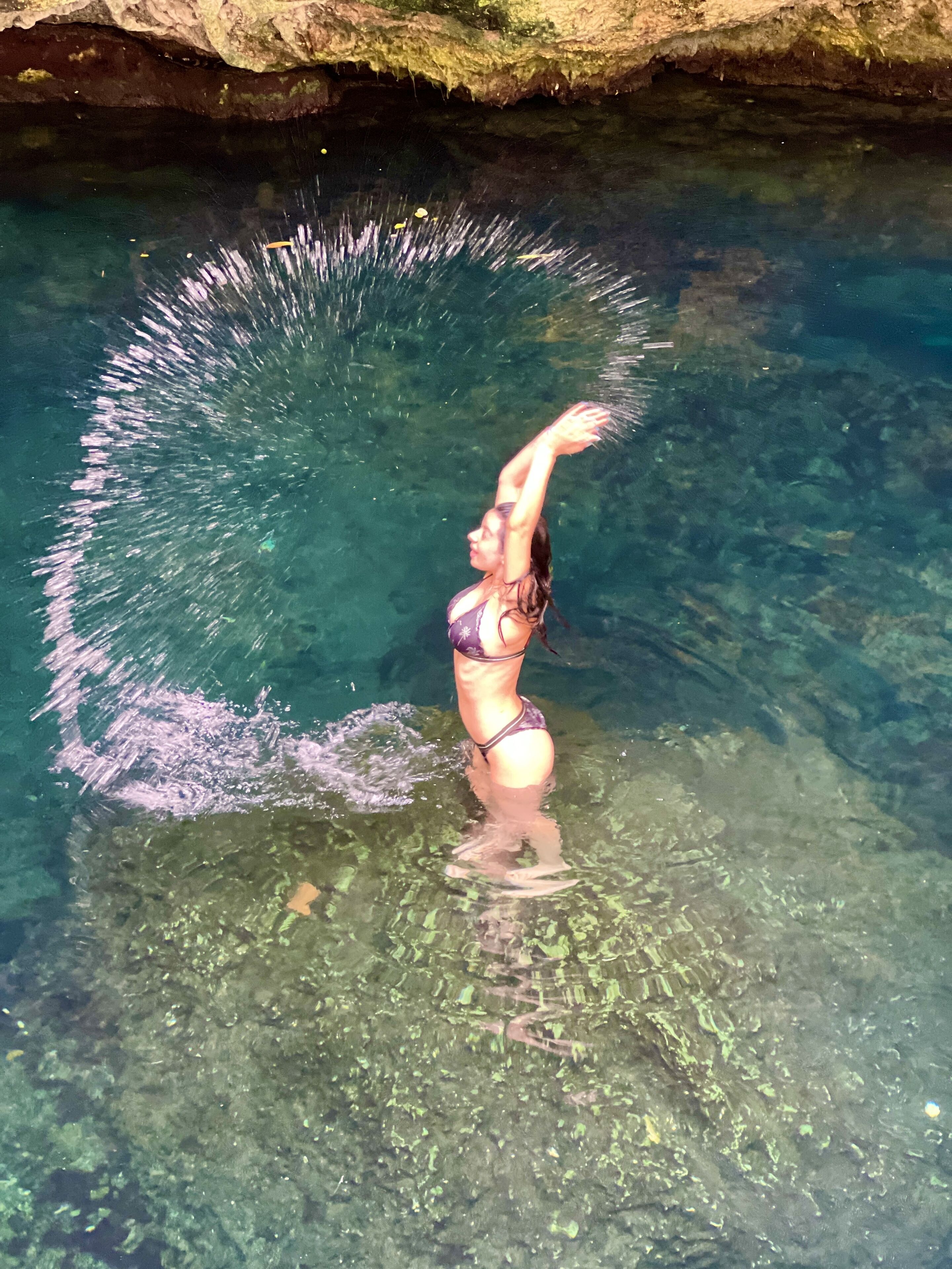 Una persona en traje de baño de pie en agua cristalina con una cueva rocosa de fondo.