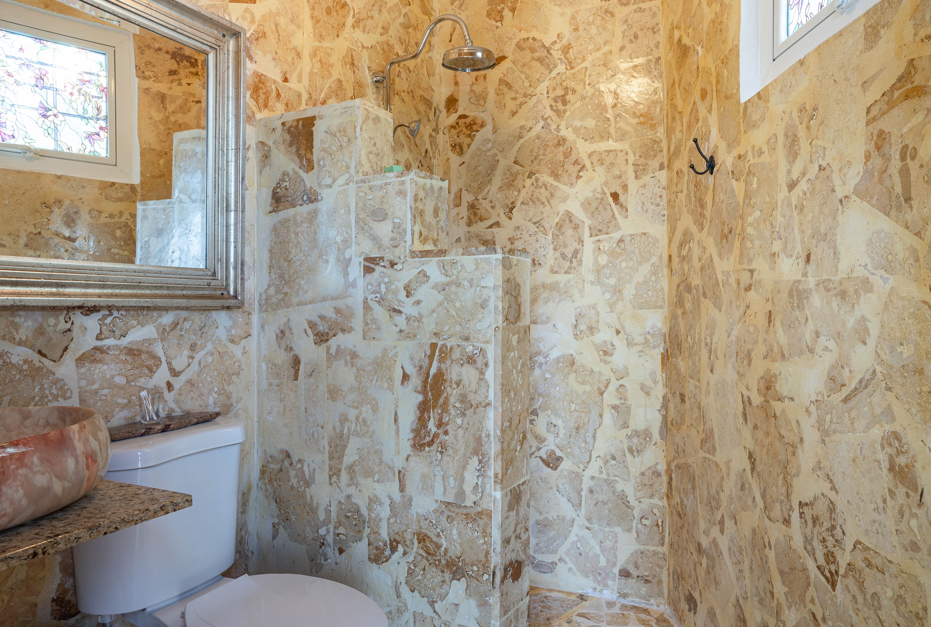 A bathroom with a stone wall, a shower, a toilet, and a sink with a large bowl.