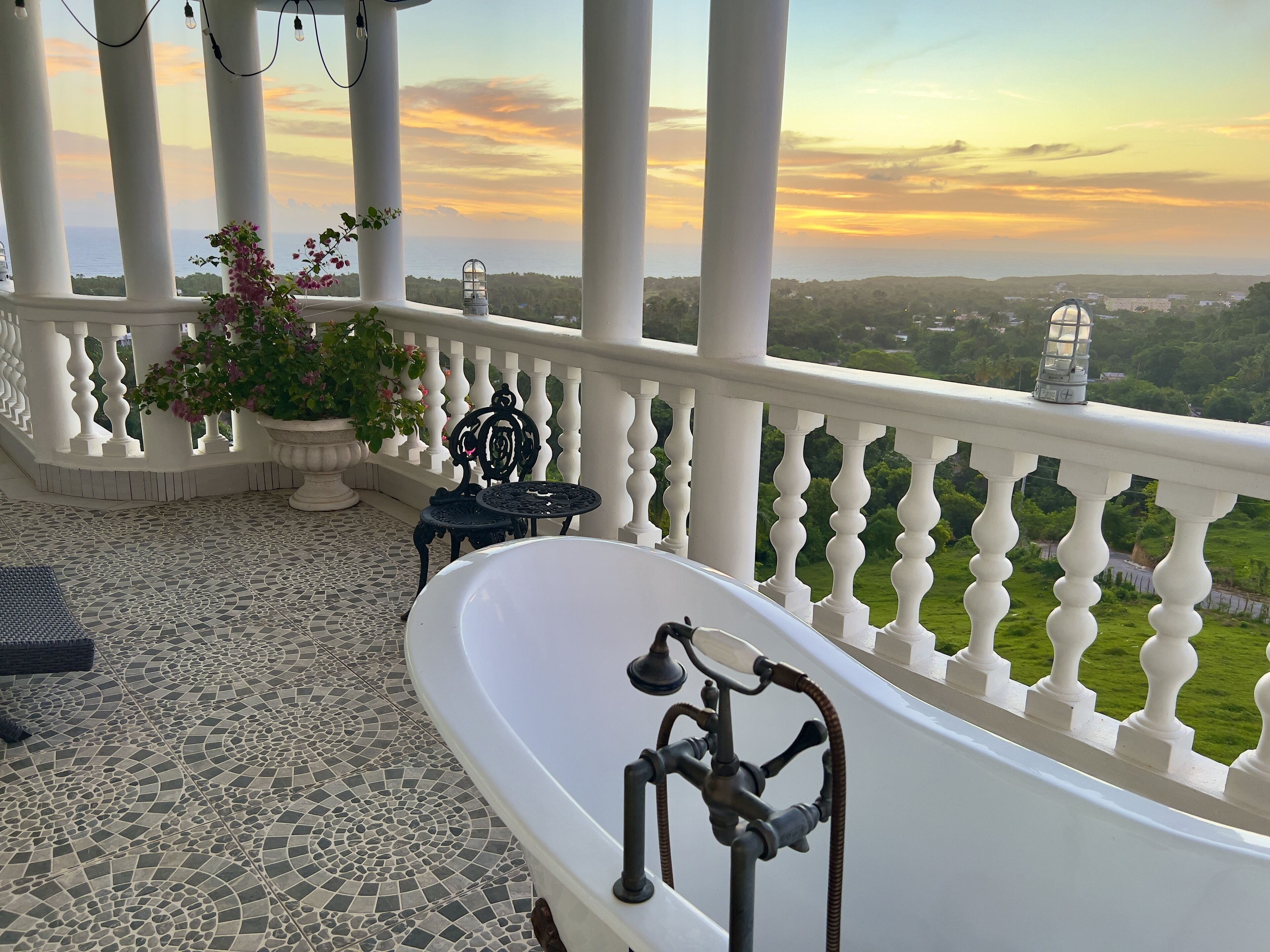 A balcony with a white bathtub, potted plants, and a view of the landscape.