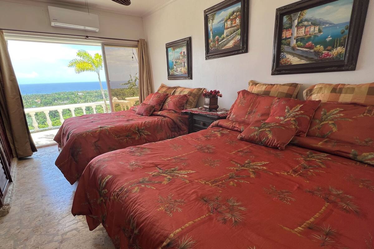 Una habitación con dos camas, un balcón con vistas al mar y dos cuadros en la pared.