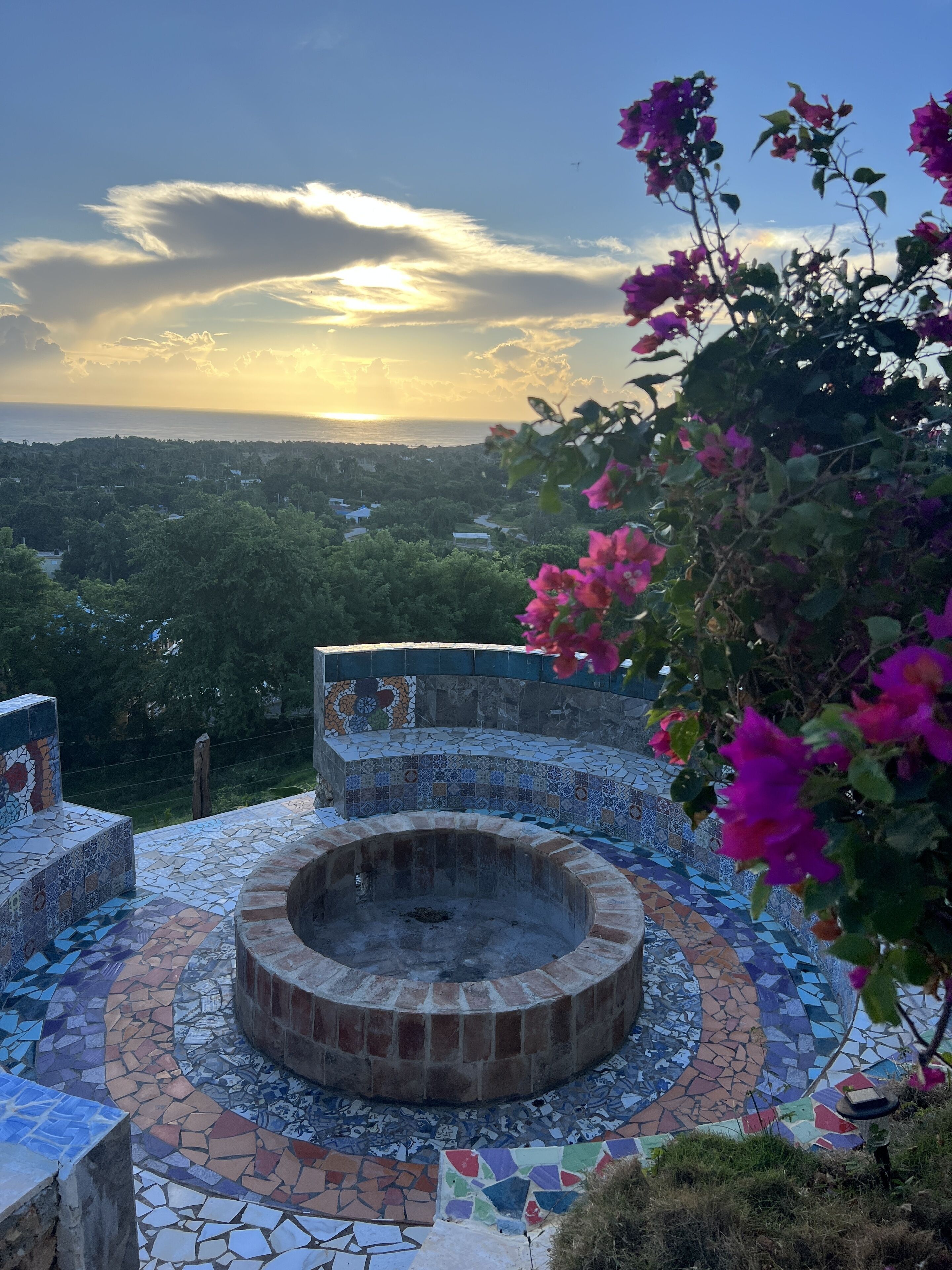 Un área de estar circular al aire libre con suelo de mosaicos, rodeada por un muro bajo con diseño de azulejos.