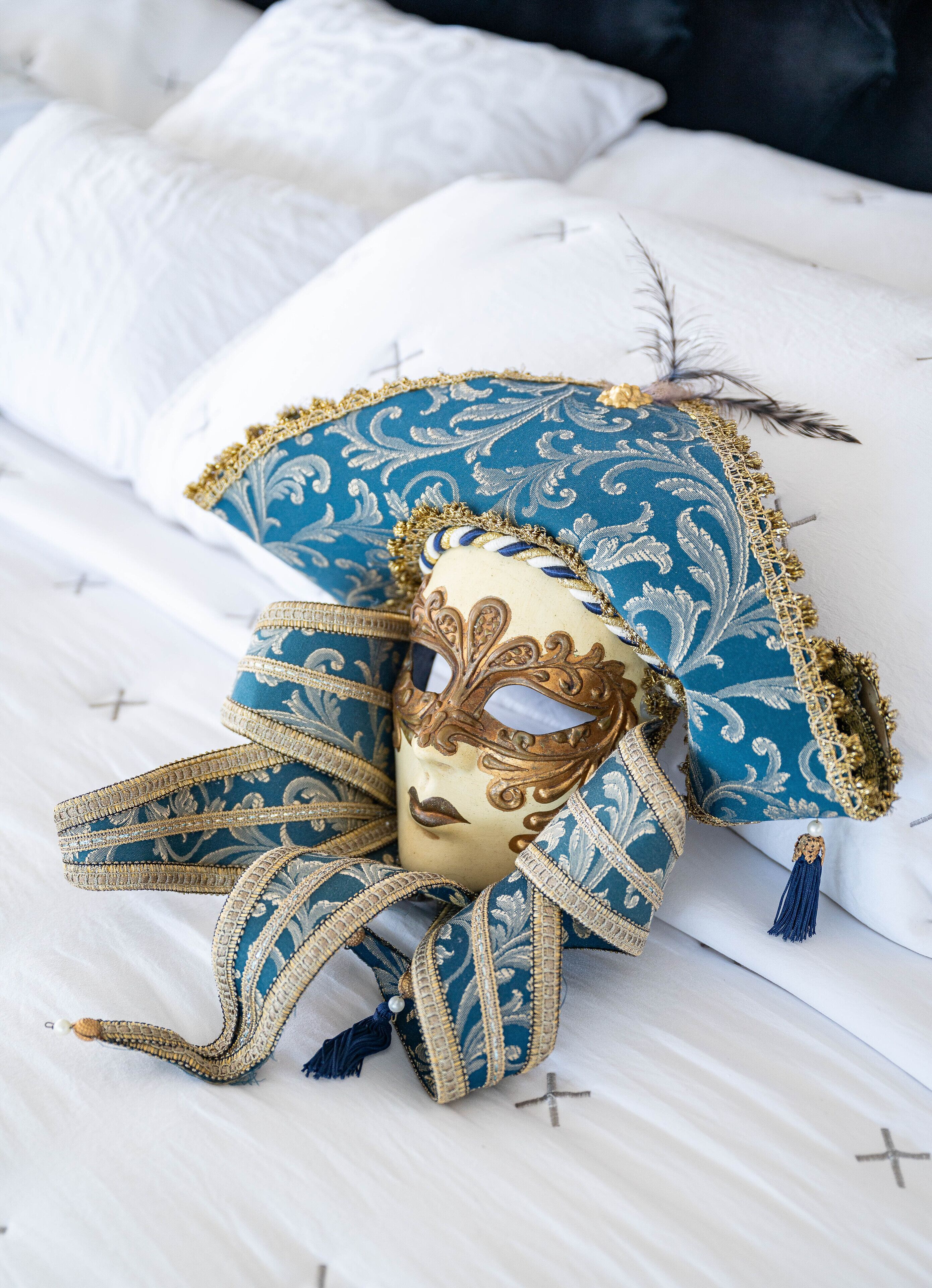 A bed with white linens, a blue and gold decorative pillow, and a mask with a tassel.