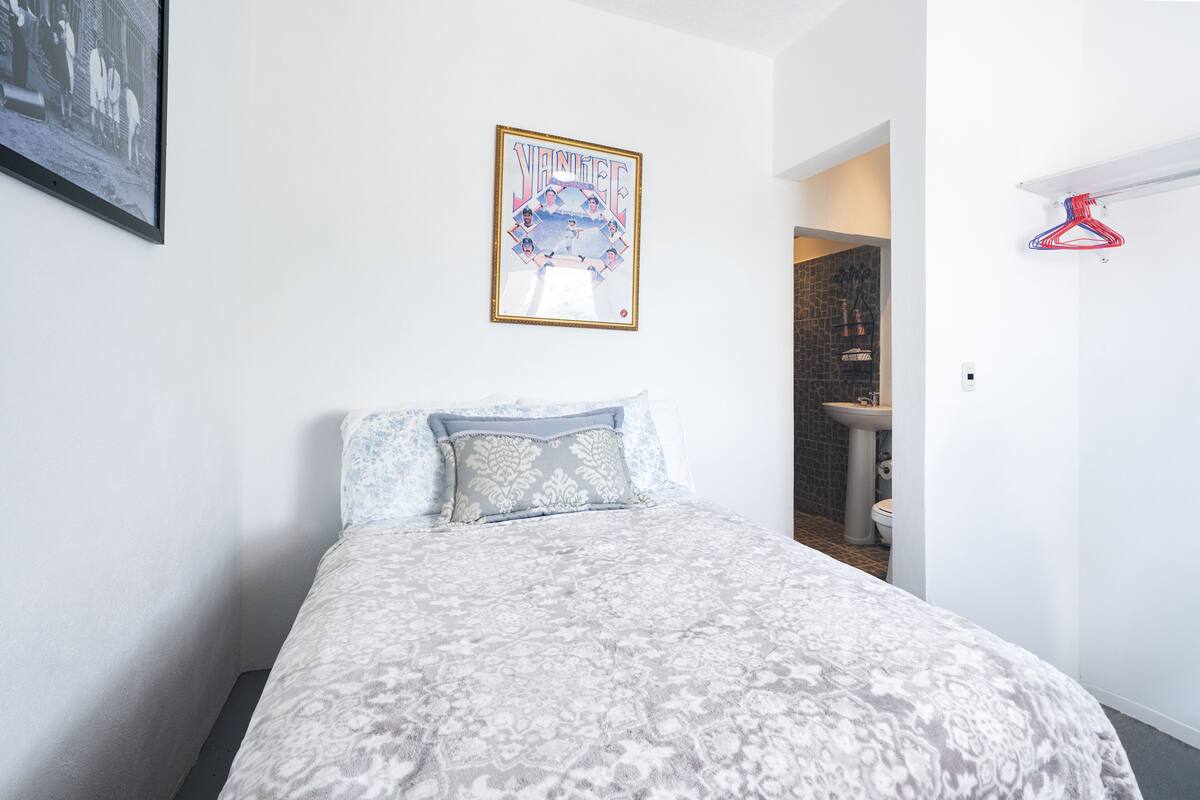 Un dormitorio con una cama, un cuadro en la pared y un baño visible a través de una puerta abierta.
