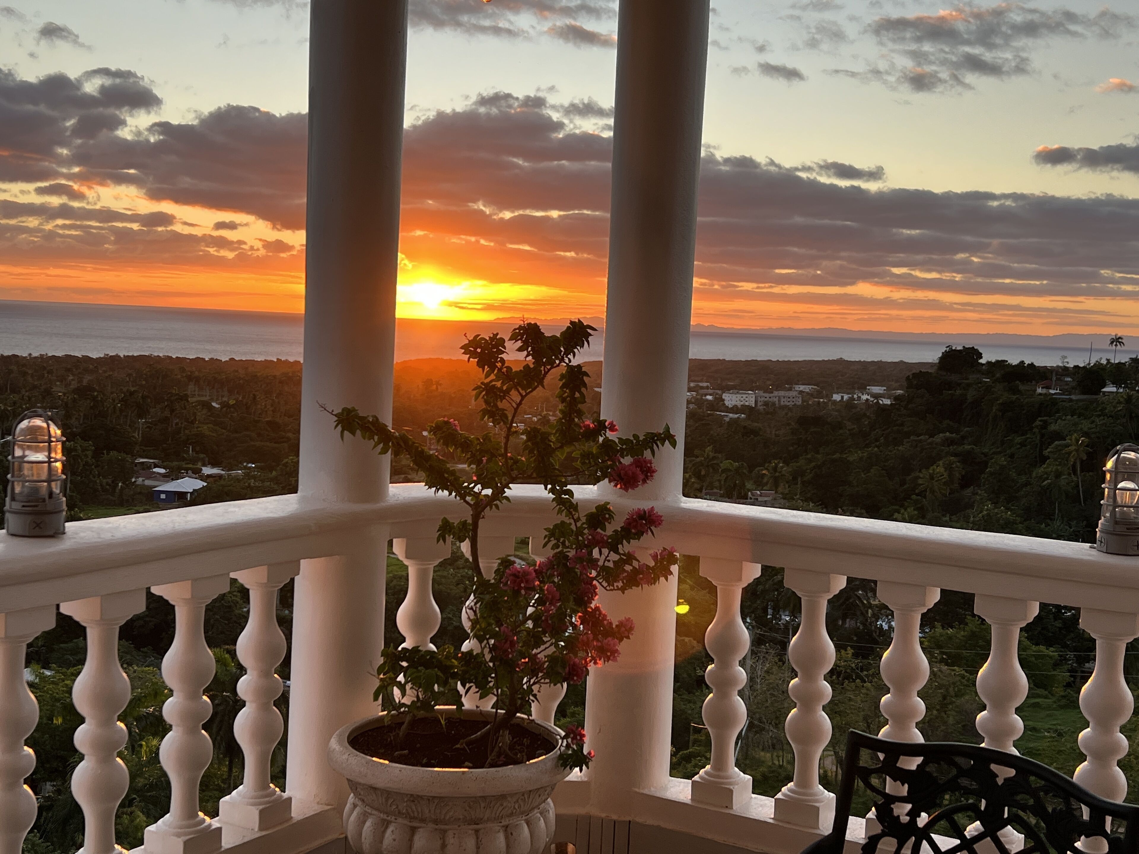 Un balcon agrémenté d’un pot de fleurs et de deux lanternes, offrant une vue sur le coucher du soleil.