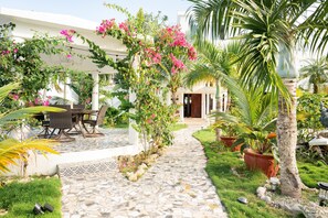 A garden pathway leading to a covered seating area with a table and chairs, surrounded by potted plants and a palm tree. - Casablanca Hotel (Cabrera)