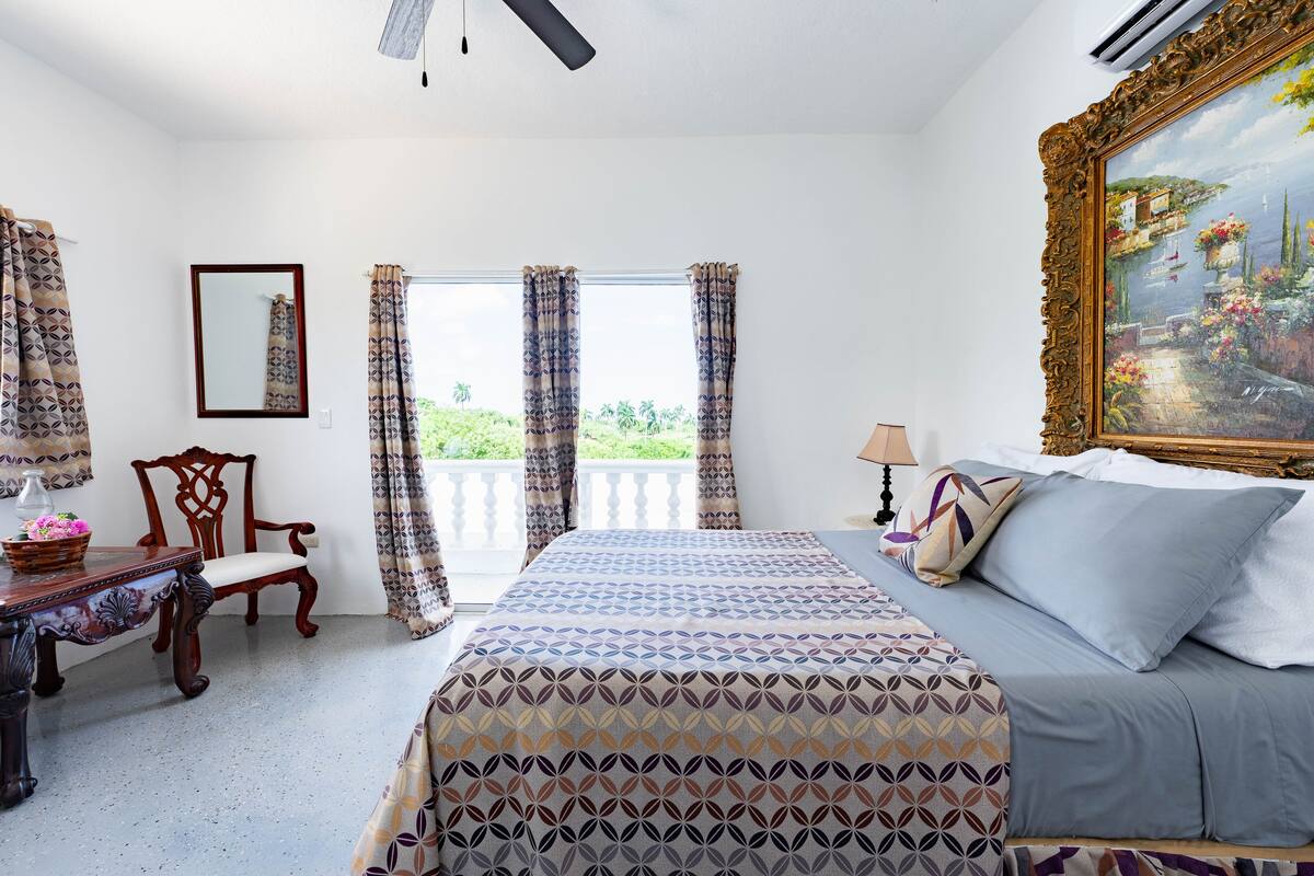 Un dormitorio con cama, escritorio, silla y balcón con cortinas.