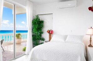 Ein Schlafzimmer mit einem großen Bett, einer Topfpflanze, einem Nachttisch und Blick auf den Ozean.
