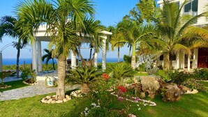 Un jardín tropical con palmeras, un pabellón blanco y vistas al océano.
