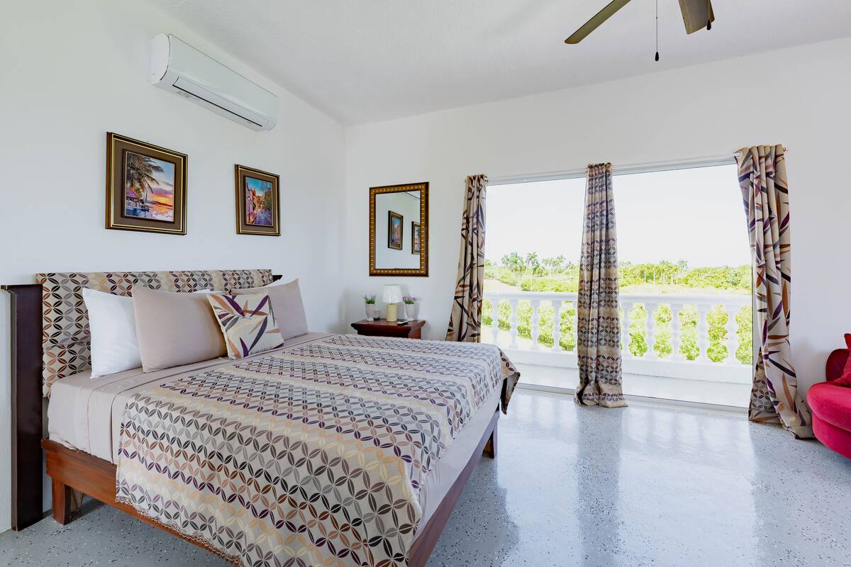 Un dormitorio con cama, mesita de noche, ventana con cortinas y balcón con barandilla.
