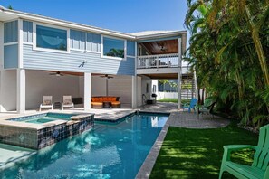 Une maison à deux étages avec une piscine, un espace salon extérieur et un balcon couvert.