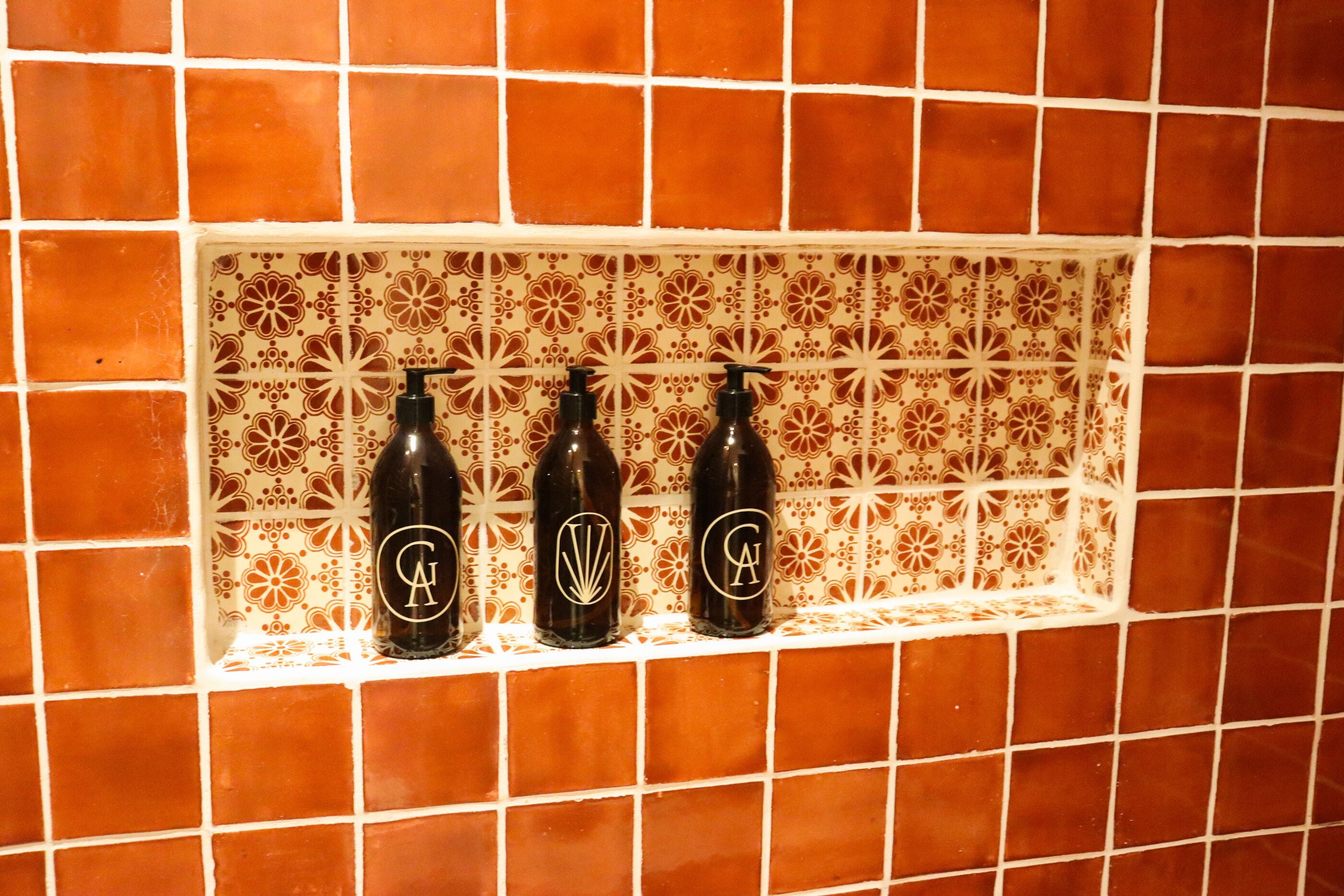 A tiled wall with a shelf holding three bottles with a logo.