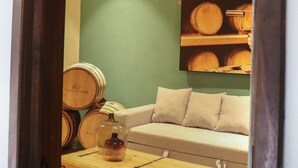 Una habitación con pared verde, sofá color beige, un cofre de madera y barriles.