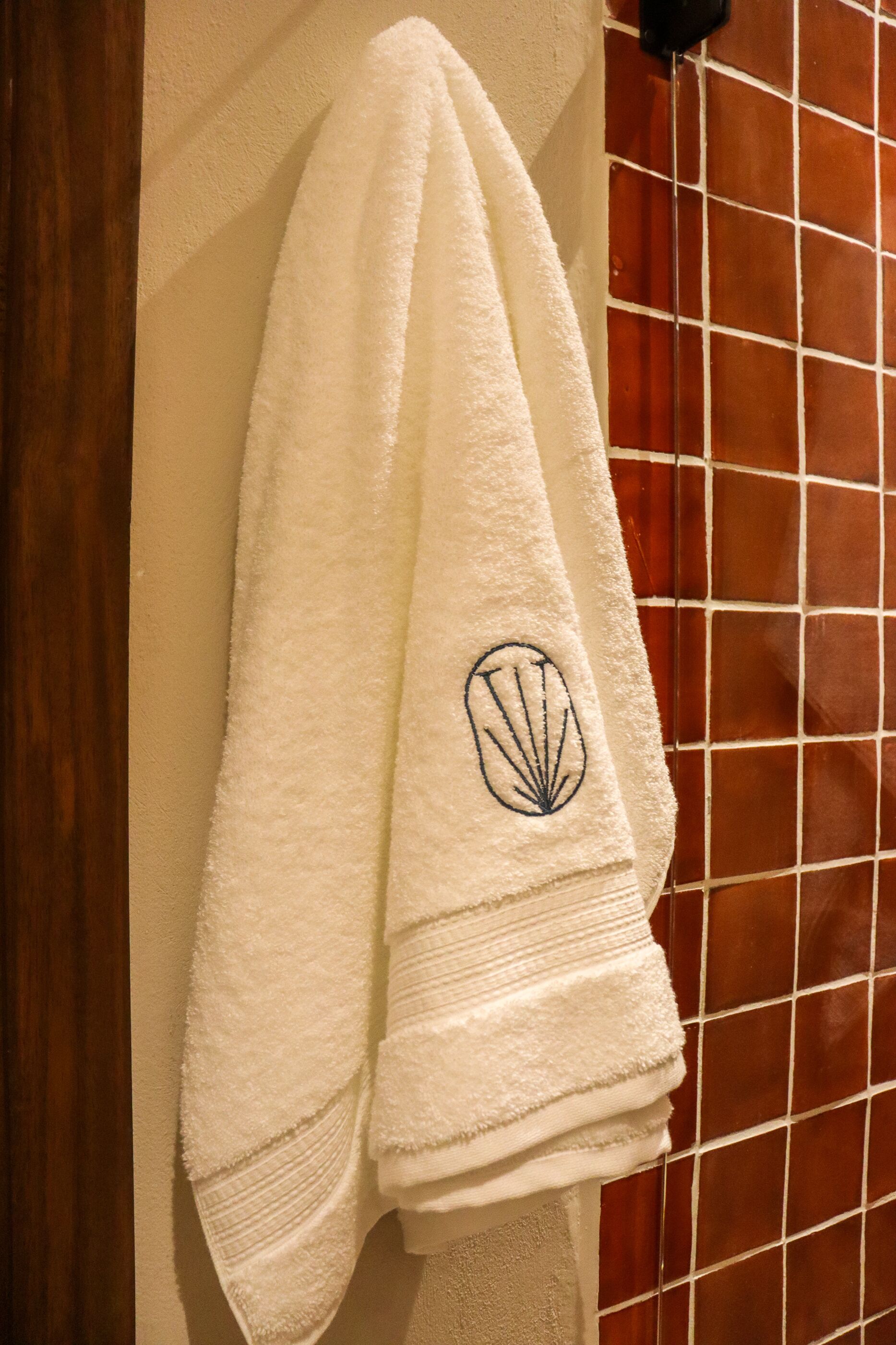 Une serviette blanche ornée d’un logo en forme de coquillage, accrochée au mur.