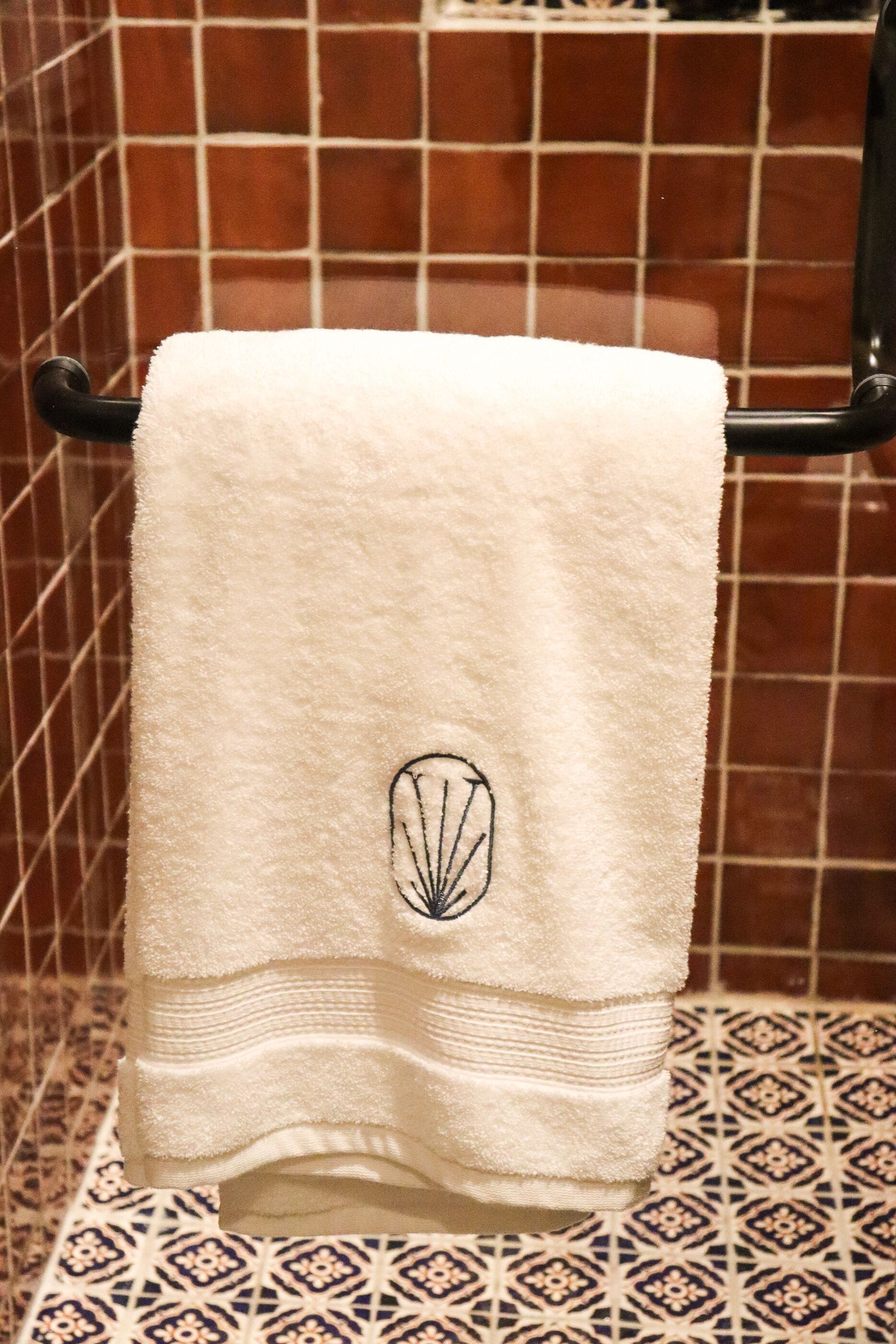 A white towel with a logo on a rack in a bathroom with patterned tiles.