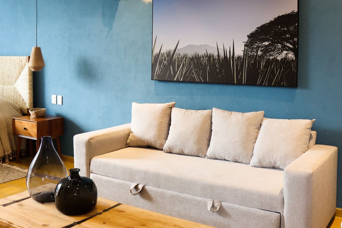 A living room with a blue wall, a light grey sofa, a wooden coffee table, and a painting of a landscape.