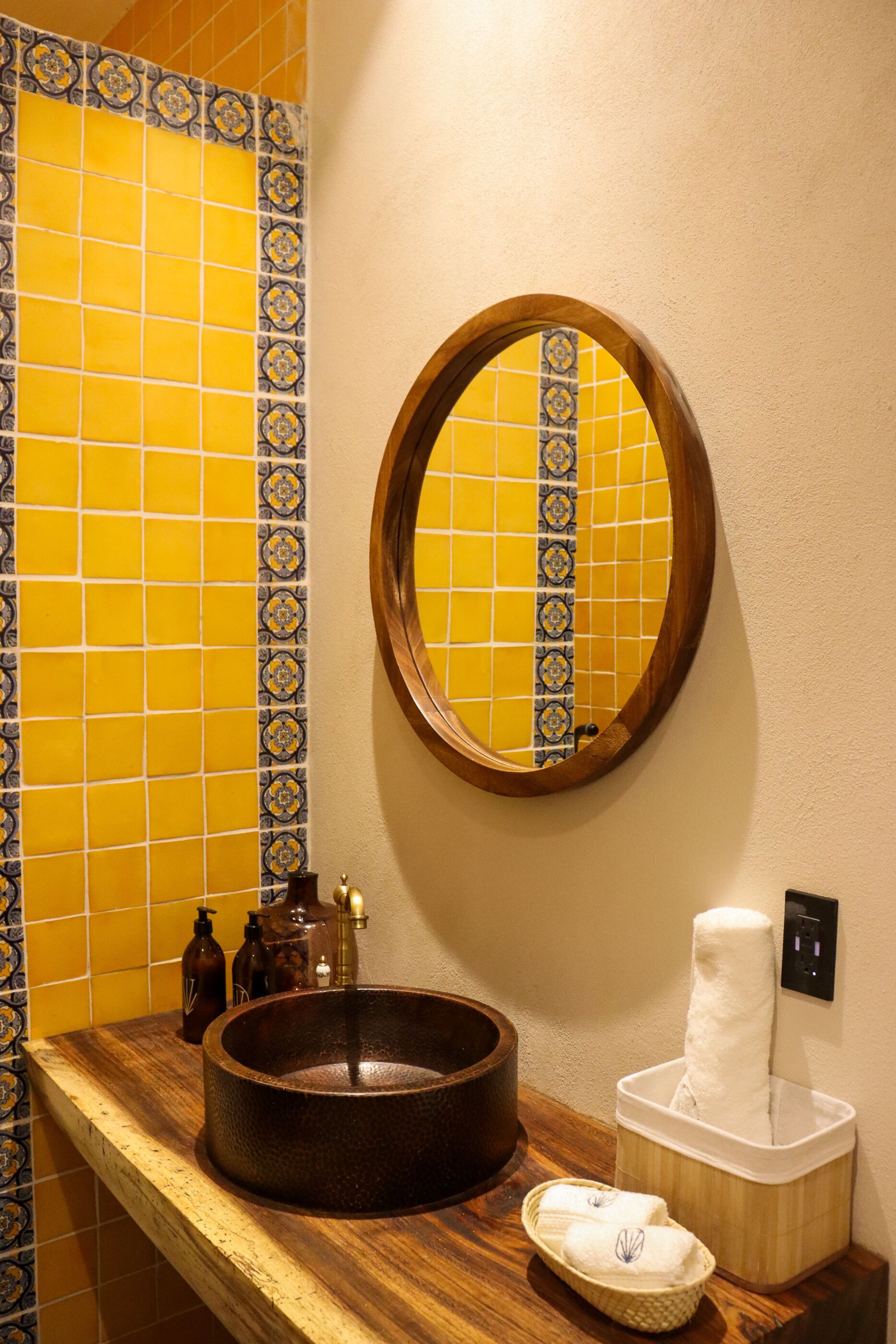 Un bagno con un mobile lavabo in legno, uno specchio rotondo, piastrelle gialle e blu a motivi decorativi, un lavandino e un dispenser di asciugamani.