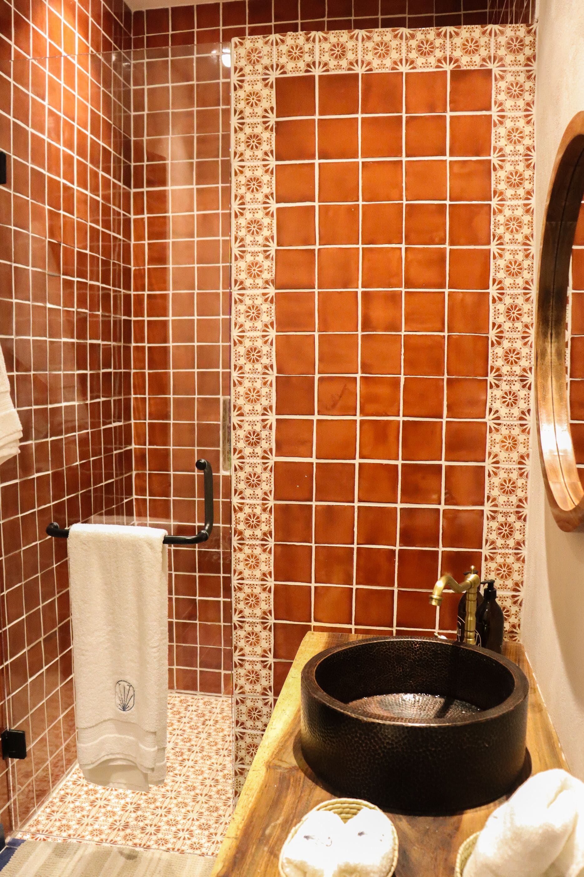 Un baño con pared de azulejos, lavamanos de madera, toallero y espejo.