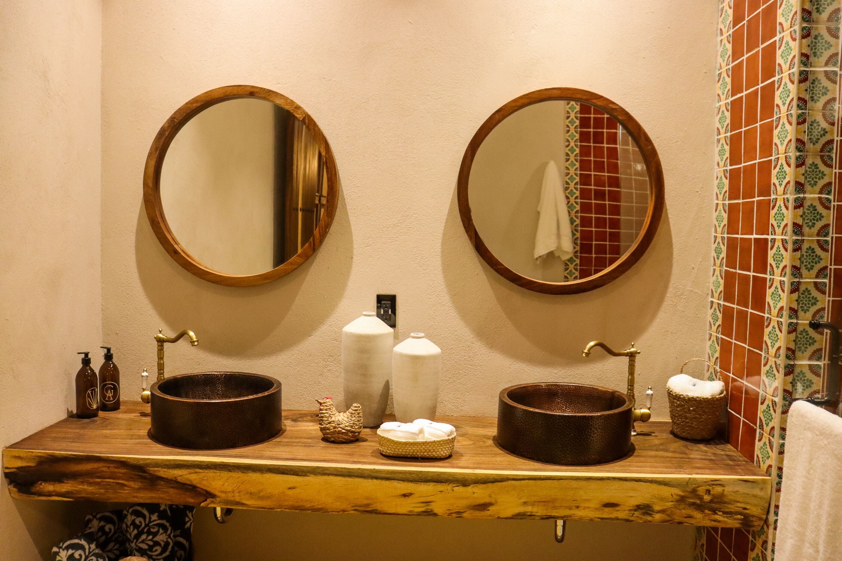 Un baño con dos espejos redondos, un tocador de madera y una zona de ducha con azulejos.