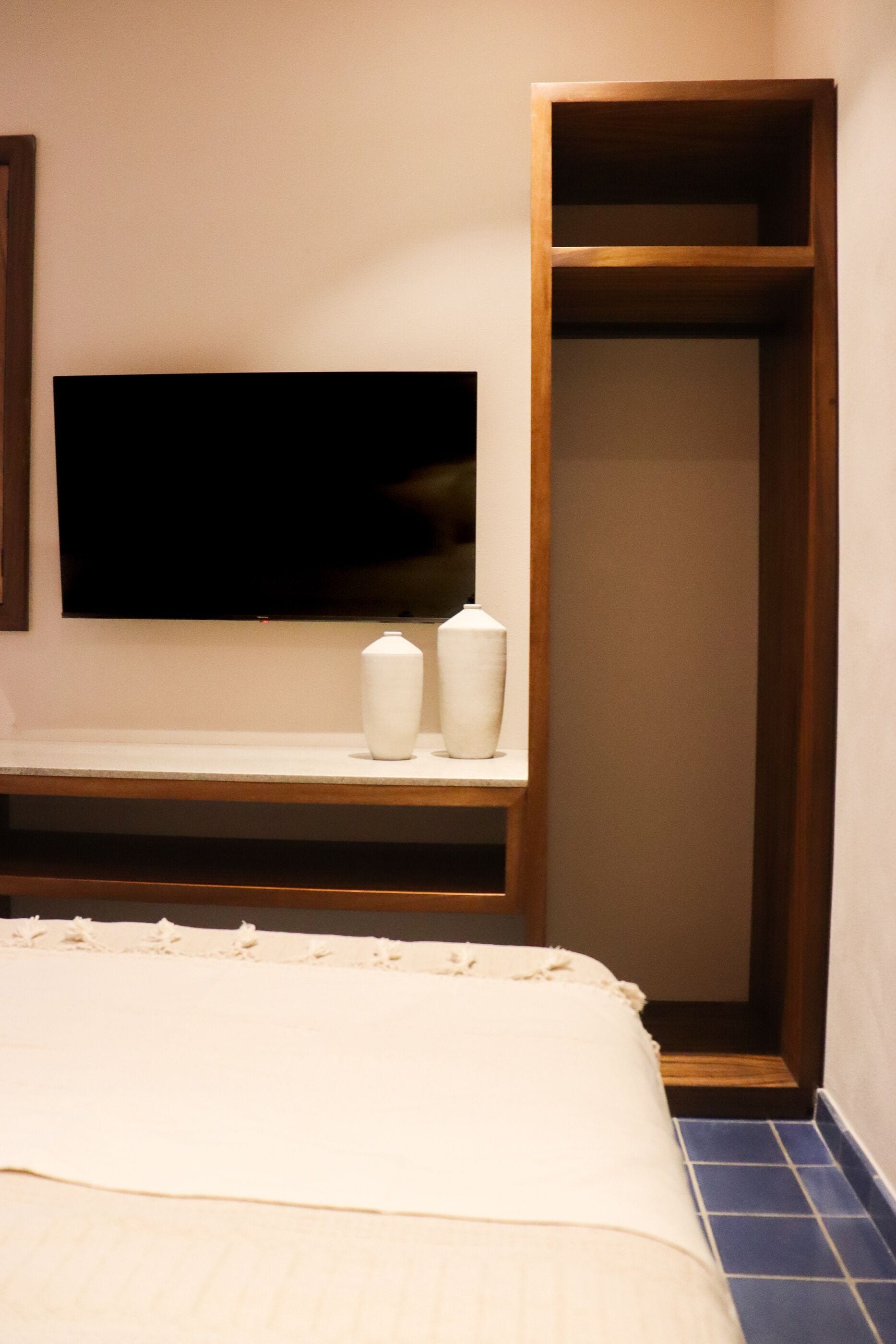 A bedroom with a bed, a TV mounted on the wall, and a wooden shelf with two white vases.