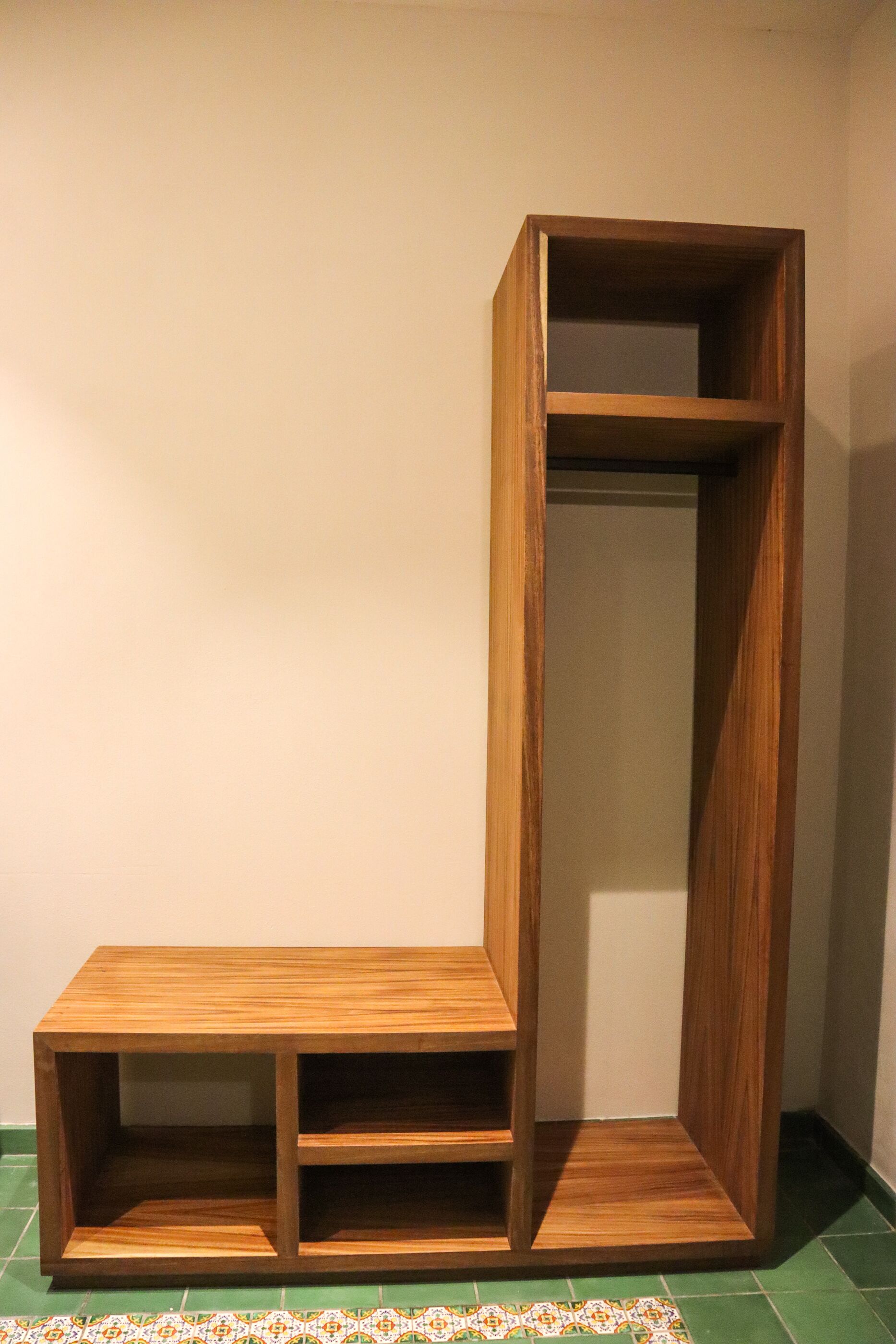 Un estante de madera con varios compartimentos, colocado frente a una pared lisa y un suelo estampado.