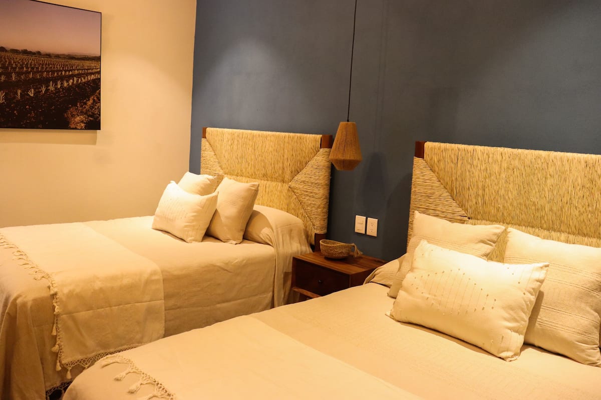 A room with two beds, each with a woven headboard, a bedside table, and a hanging lamp.