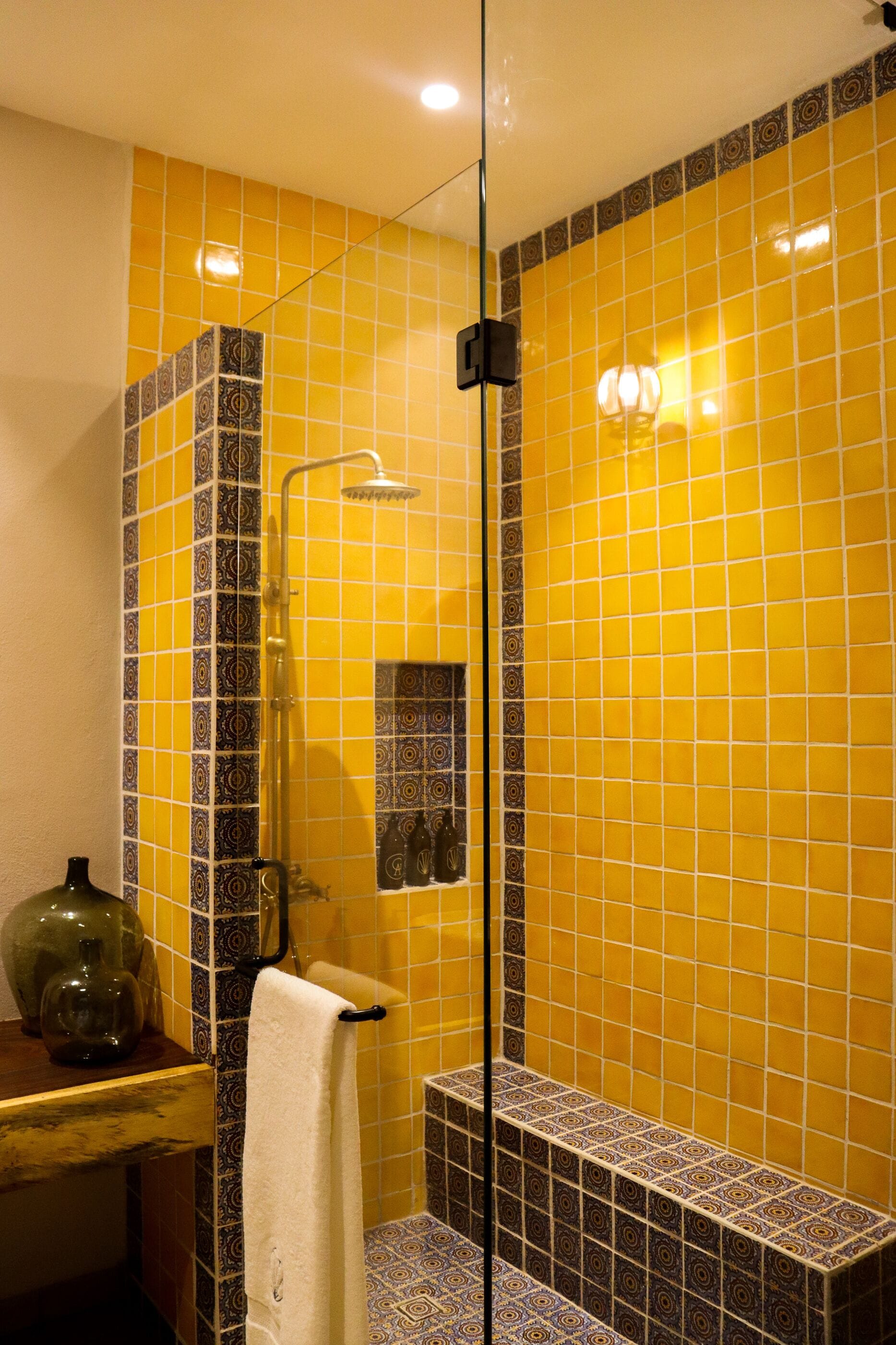 Un baño con paredes de azulejos amarillos, una cabina de ducha de vidrio y un mostrador de madera con una toalla.