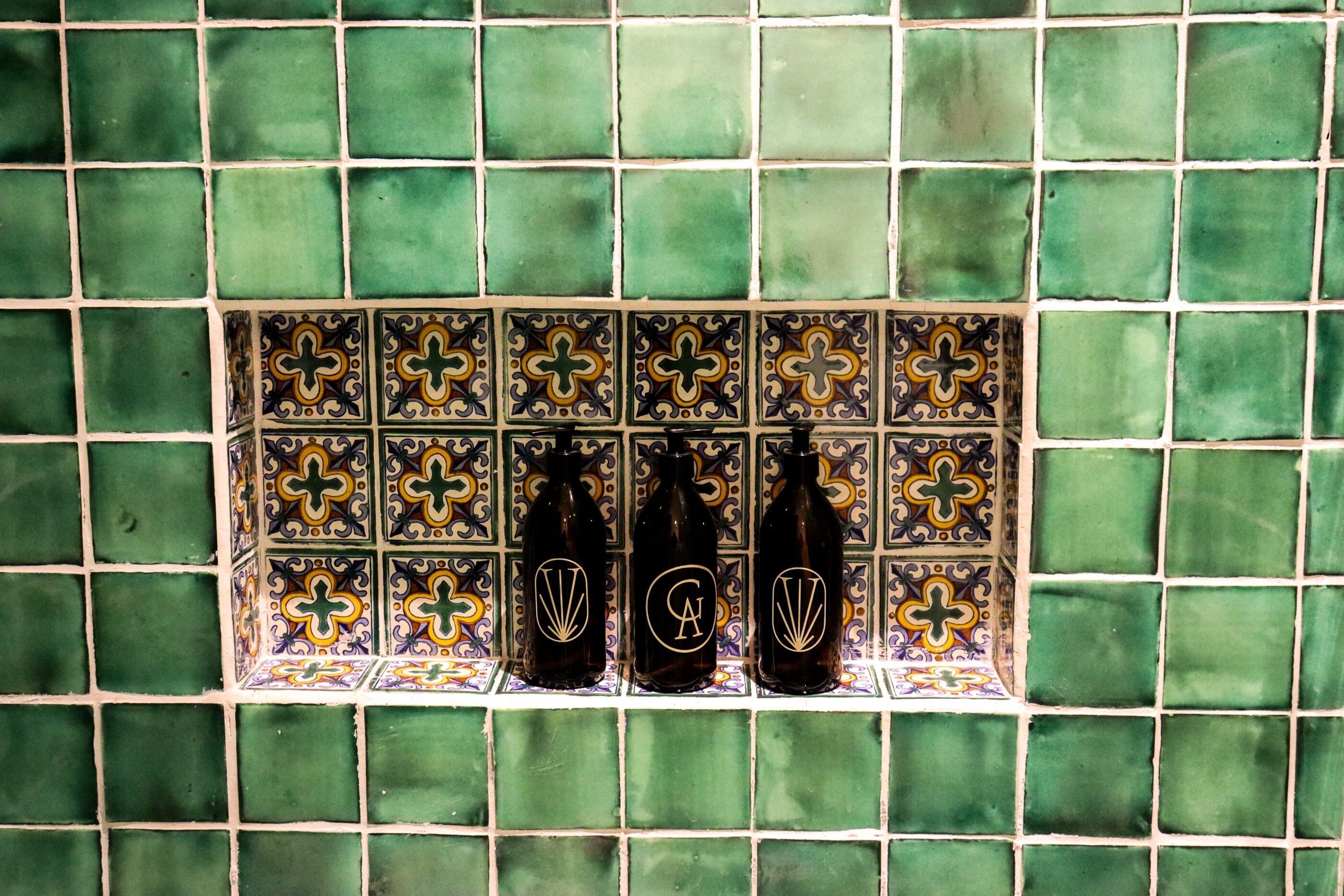 A tiled wall with three bottles in a shelf.