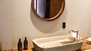 Un baño con tocador de madera, espejo redondo, lavamanos de piedra y dos dispensadores de jabón.