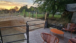 Un terrazzo in legno con ringhiera metallica, circondato da un giardino con alberi e una recinzione.