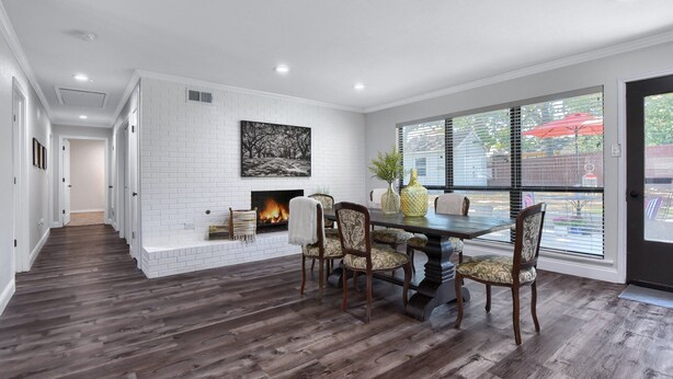 A spacious living room with a fireplace, a dining area with a table and chairs, and large windows with blinds. - The Sophey (Denison)