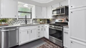 A modern kitchen with white cabinets, stainless steel appliances, and a herringbone patterned backsplash. - The Sophey (Denison)