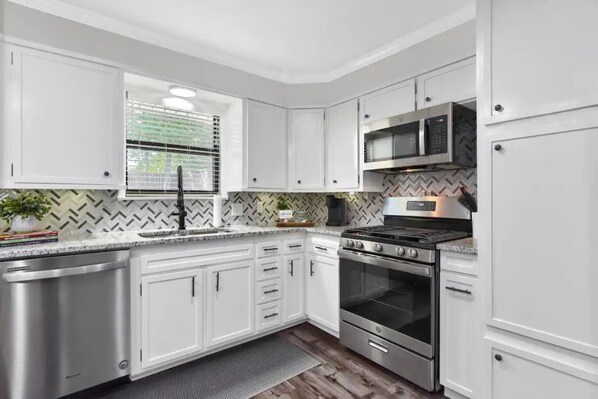 A modern kitchen with white cabinets, stainless steel appliances, and a herringbone patterned backsplash. - The Sophey (Denison)