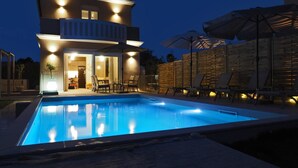 Una casa de dos pisos con piscina, mobiliario exterior y un cerco de madera.