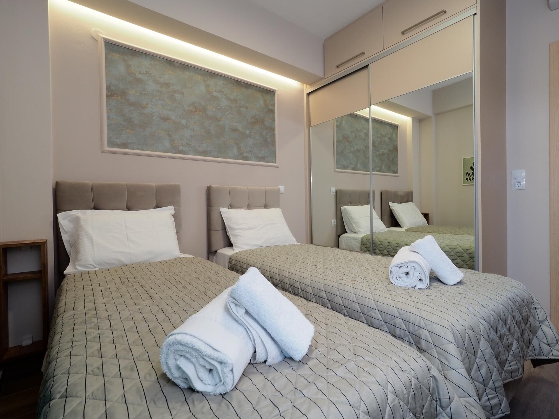 Een hotelkamer met twee bedden, elk met een gewatteerde spreidek en passend kussen. Tegen een muur hangt een grote spiegel en boven de bedden een lijst met een abstract schilderij.