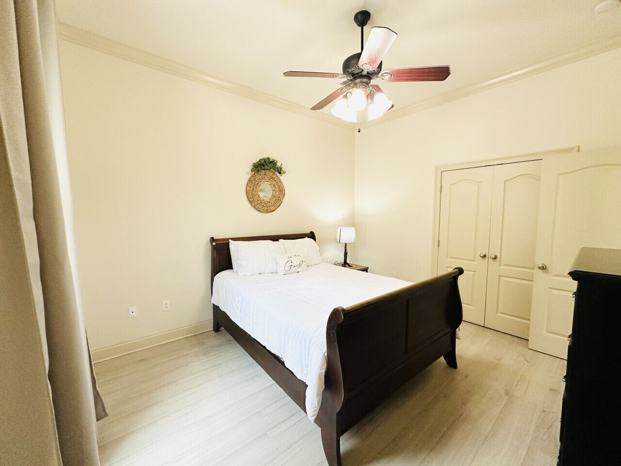 Une chambre à coucher comprenant un lit, un ventilateur de plafond, une lampe fixée au mur, une porte et une poubelle.