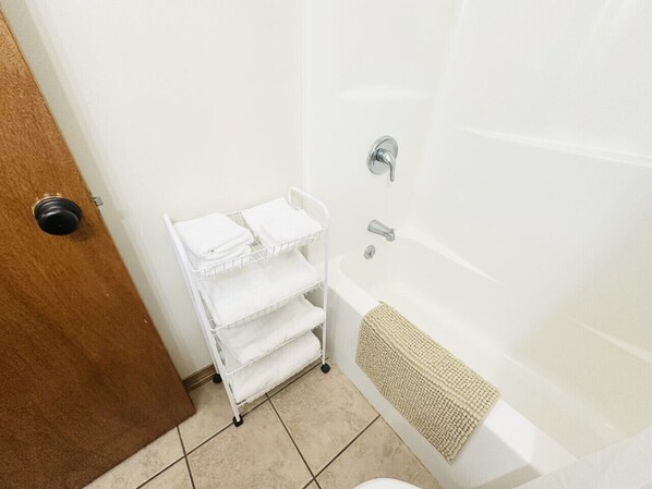 A bathroom with a white bathtub, a towel rack with folded towels, and a door with a round handle.