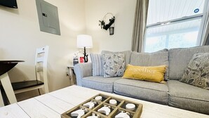 A living room with a grey sofa, a wooden coffee table with a puzzle, a lamp, and a decorative wall hanging.