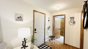 A room with a white door, a small table with a lamp, a chair, and a checkered rug.
