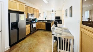 Una cocina moderna con armarios de madera, electrodomésticos de acero inoxidable y un comedor con mesa y sillas blancas.