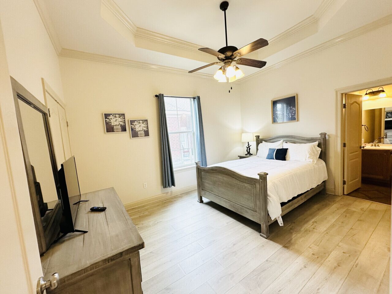 A bedroom with a bed, a ceiling fan, a window with curtains, a bedside table, and a mirror.
