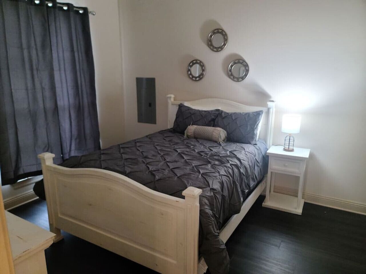 A bedroom with a bed, a nightstand, a lamp, and a wall-mounted mirror.