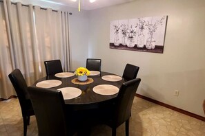 A dining area with a round table, black chairs, and a vase with yellow flowers.