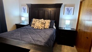 Une chambre avec une tête de lit en bois foncé, une couvre-lit matelassé, deux tables de chevet avec des lampes et une porte sur le côté droit.