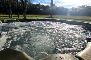 A hot tub with water jets in motion, surrounded by a grassy area with trees in the background. - Stewart House with Hot Tub and 3 bedroom (Tickfaw)