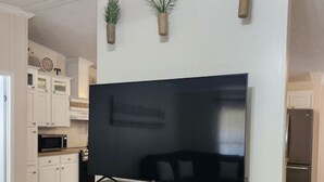 A modern kitchen with white cabinetry, a large flat-screen TV mounted on a wooden cabinet, and three hanging plants. - Thomas House, spacious house in Tickfaw, LA (Tickfaw)