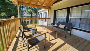 A covered outdoor deck with wooden flooring, metal-framed tables and chairs, and a bench. - Thomas House, spacious house in Tickfaw, LA (Tickfaw)