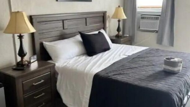 Une chambre à coucher comprenant un lit, deux tables de chevet avec des lampes, un ventilateur de plafond, une fenêtre avec des rideaux et un tapis à motifs.