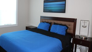 A bedroom with a large bed, a nightstand, a wall-mounted light fixture, and a window. - Delightful 3-bedroom house in Bradenton with WiFi, Games, and more #2 of 2 (Bradenton)