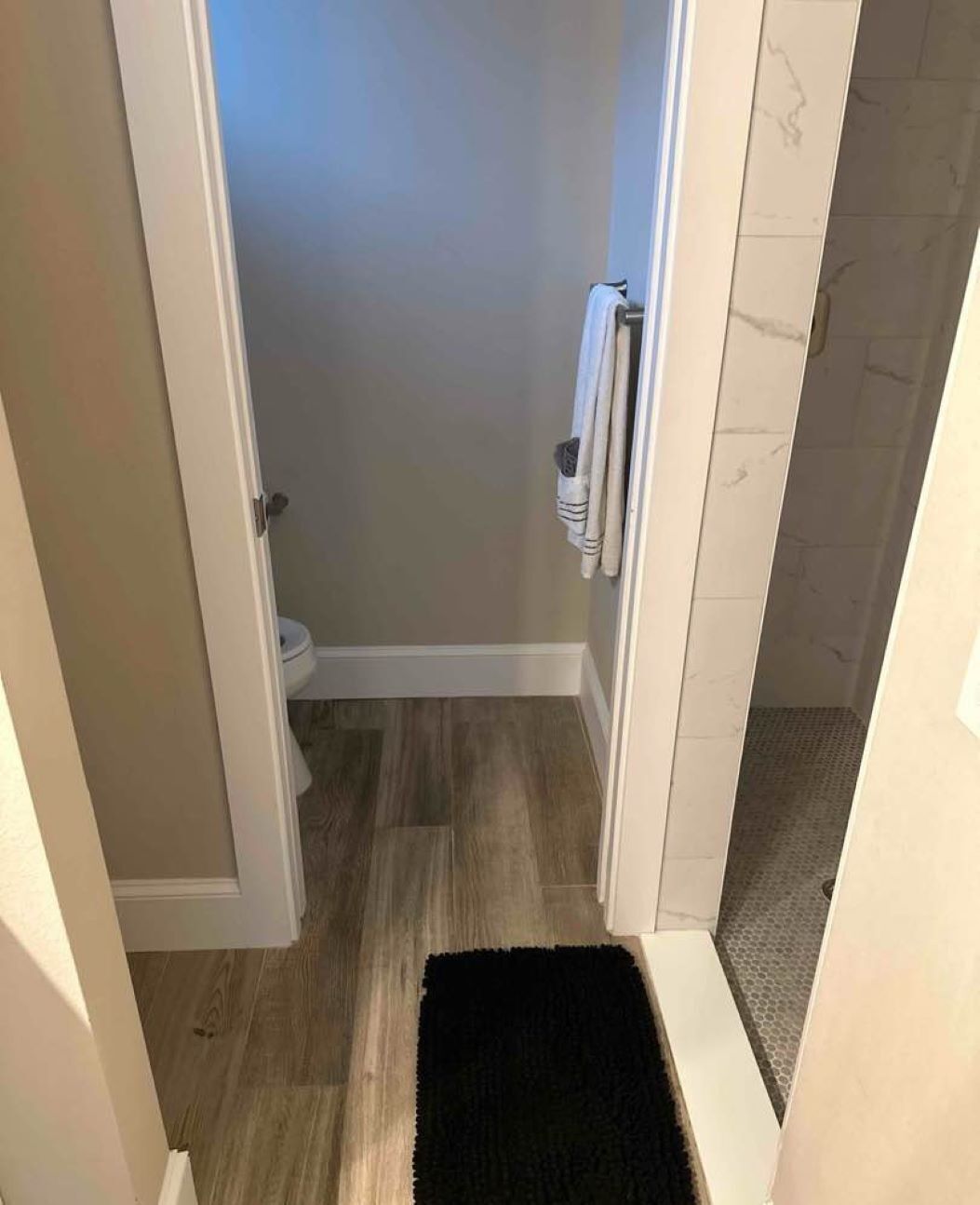 Een smalle gang met een douche, toilet en radiator.